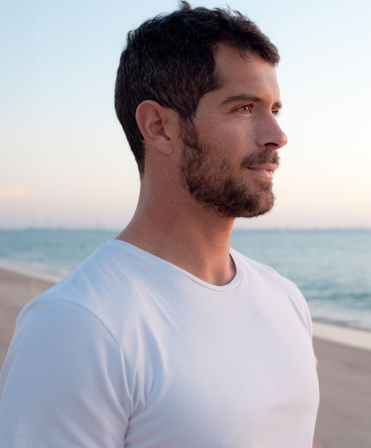 Man in white shirt by the beach at sunset.