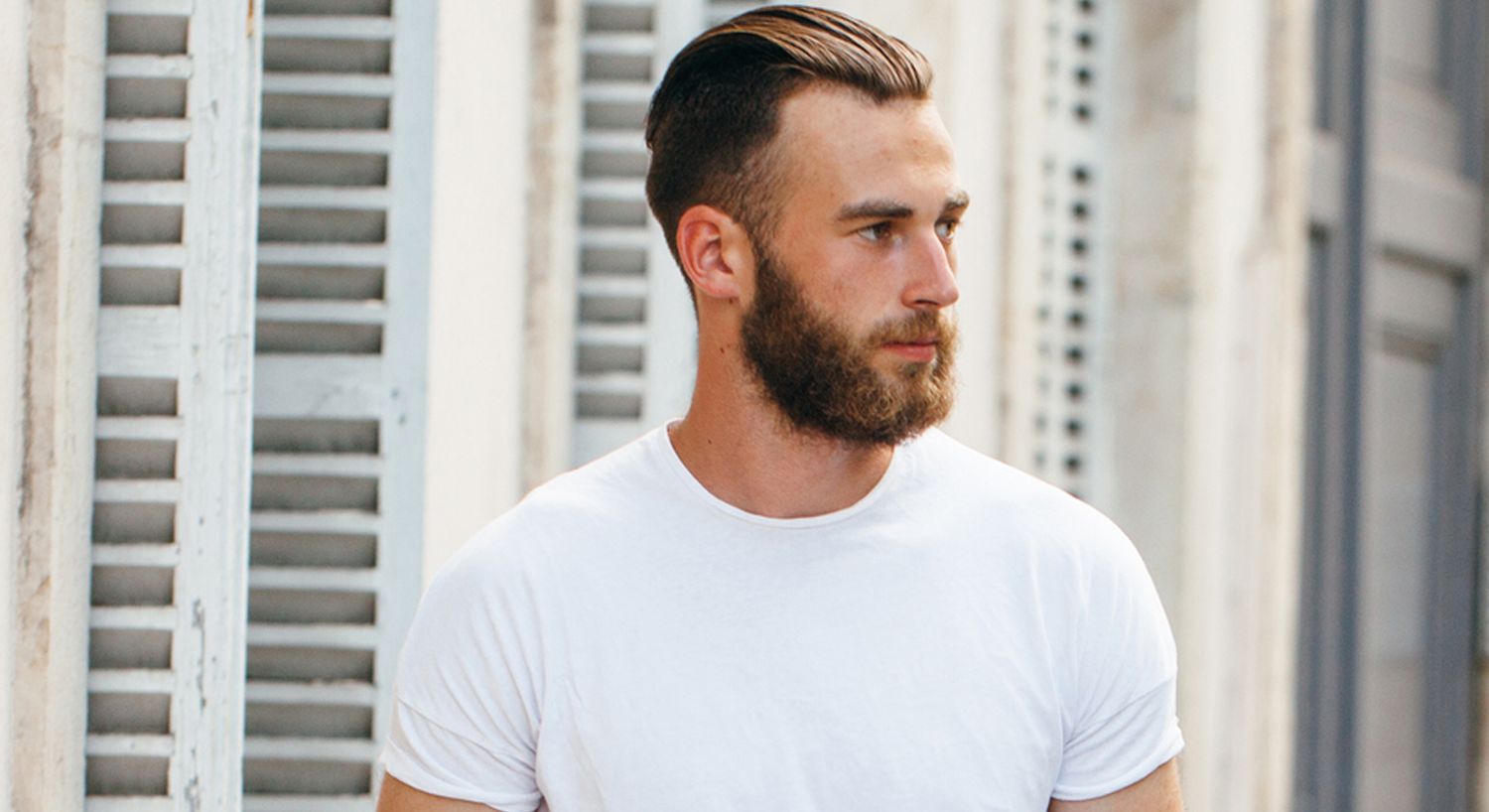 Man with beard wearing a white t-shirt outdoors.
